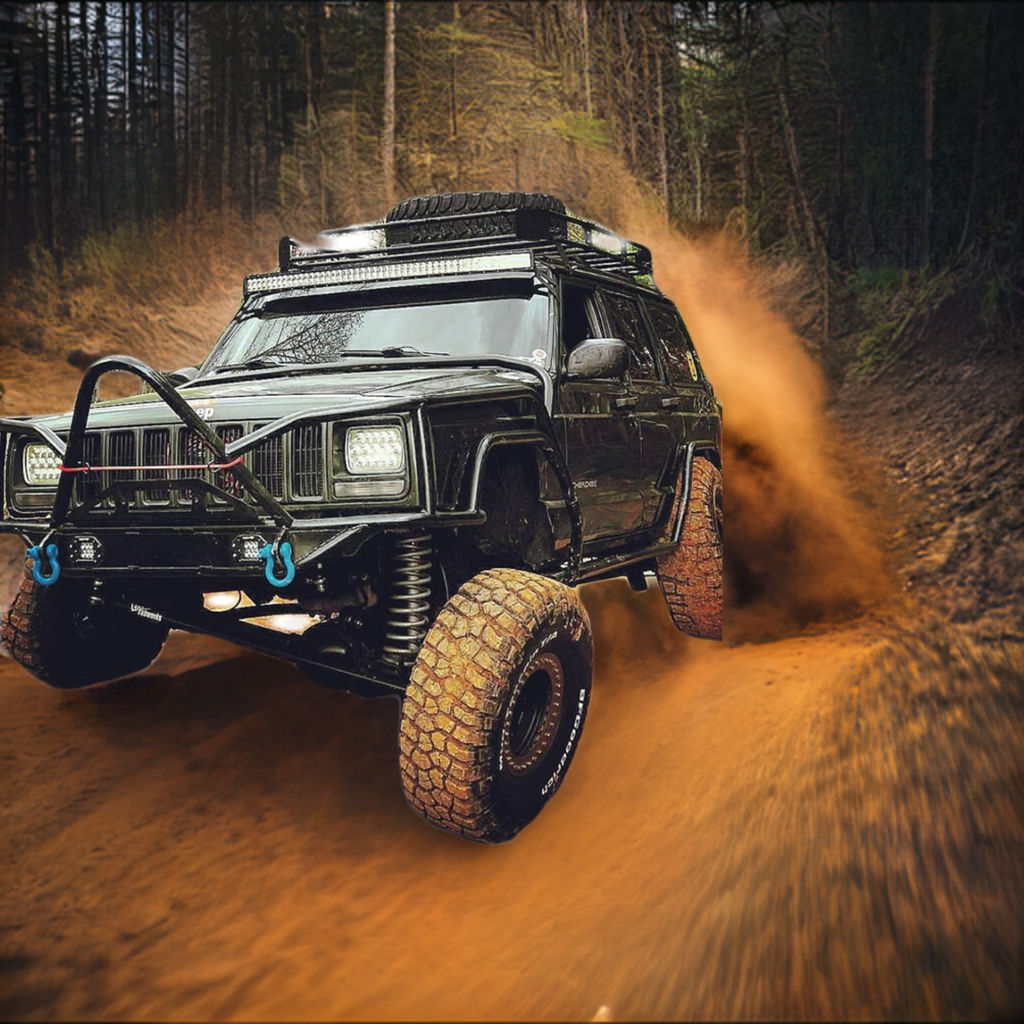 Lifted Jeep Cherokee XJ tearing through a dirt trail with aggressive off-road tires, upgraded suspension, and BKFabworks front bumper and components