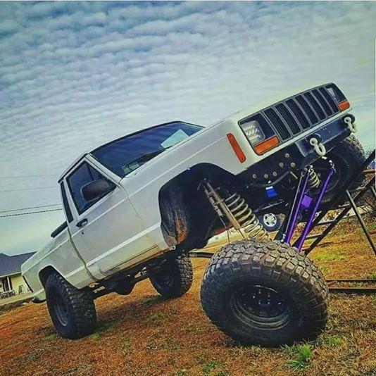 Jeep Comanche flexed out on RTI ramp with BKFabworks crossover steering and long-arm suspension kit installed, showing extreme articulation and off-road capability