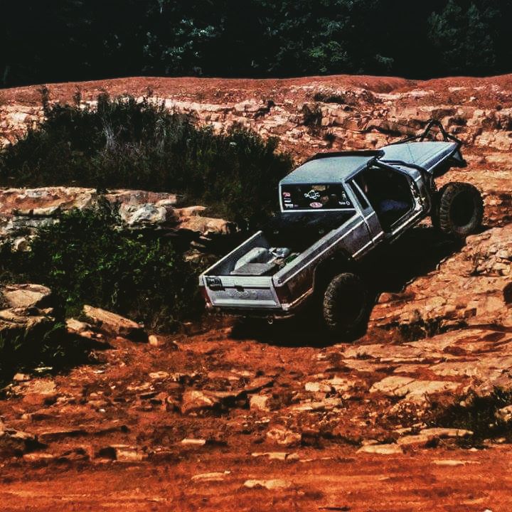 Modified Jeep Comanche MJ with BKFabworks suspension components rock crawling a red dirt trail with cage, long arms, and stripped doors.