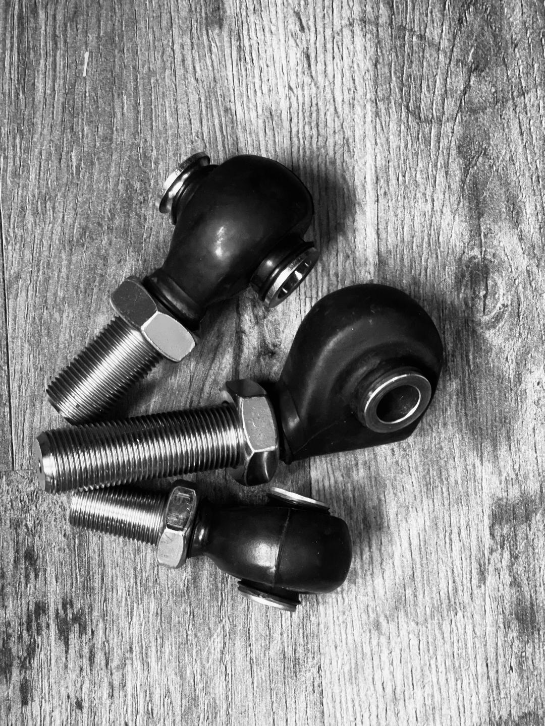 Three BKFabworks heim joints with rubber protective boots for steering and suspension applications, shown in different sizes on wood background