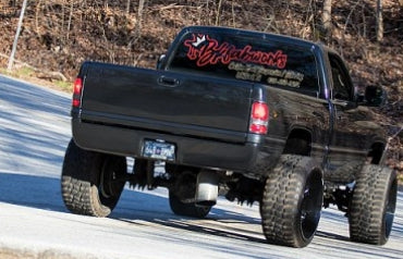 Lifted Dodge Ram truck with BKFabworks rear window decal driving on road with oversized tires and custom suspension